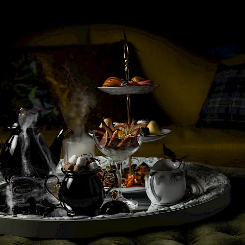A spooky hookah-style tea set with smoking pots and a tiered platter of food and sweets on a tray.