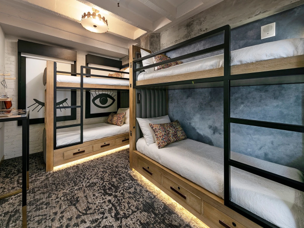 A compact dorm-style room with two black metal bunks, under-bed drawers, a mirrored wardrobe, a desk, and a patterned carpet, all in a modern, industrial vibe.