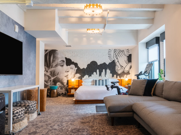 A chic, spacious loft suite with a large gray sectional, king bed, mural wall, wall-mounted TV, and a cozy lounge area by the window, bright and stylish.