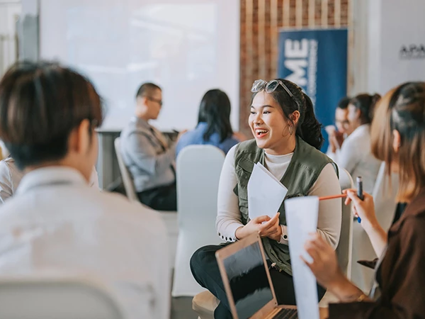 A group of people in a casual meeting or conference, chatting and sharing documents in a bright, modern space. Top it at 140 characters, always ending the sentence.