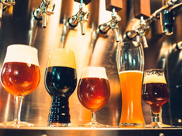 A row of diverse beer glasses on a bar counter, with taps in the background, showcasing different colors from pale to dark ales.