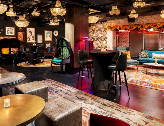 A stylish lounge or bar with warm lighting, eclectic seating, patterned rugs, chandeliers, and a cozy, artsy vibe.