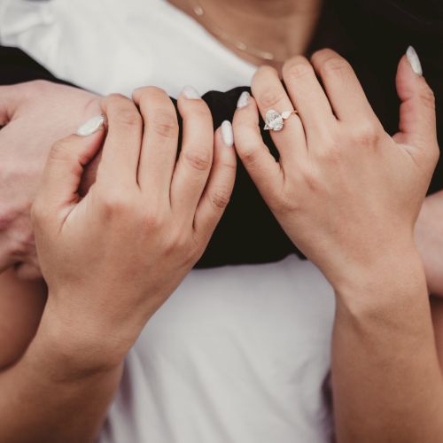 A couple&rsquo;s arms wrapped around each other, hands showing a ring on one finger. The scene feels intimate, romantic, and affectionate.