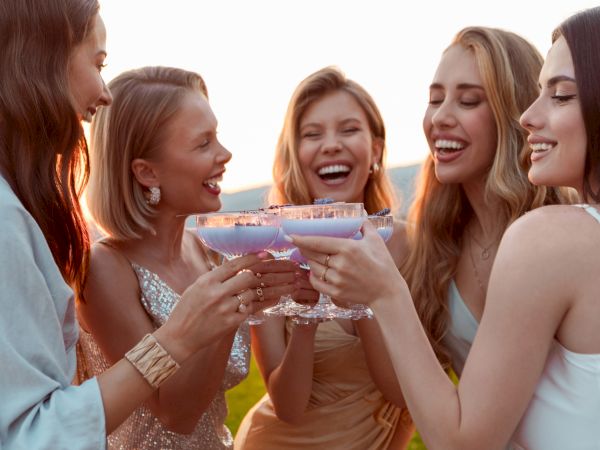 A group of five friends cheers with a colorful cocktail or cupcake, sharing a fun moment outdoors as they celebrate together.