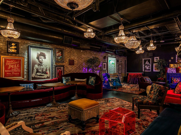 A cozy, eclectic lounge with vintage chairs, warm lighting, ornate carpets, and quirky art on brick walls, perfect for relaxing conversation.