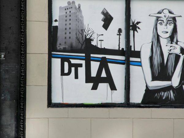 A mural shows a stylized woman in a hat beside urban graffiti elements and the letters &ldquo;DTLA,&rdquo; capturing a moody downtown vibe.