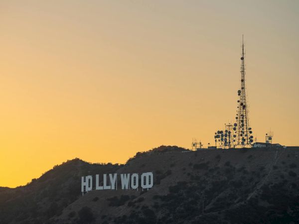 A sunset over the Hollywood Hills with the classic HOLLYWOOD sign and a tall communications tower perched on the ridge.