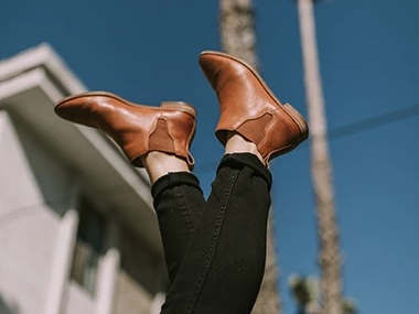 A person&rsquo;s legs in tan boots stuck in the air against a blue sky, palm trees, and buildings in the background.
