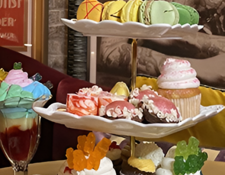 A tiered dessert platter with colorful cupcakes, macarons, candy toppers, and a rainbow flag; sweet treats overflow the plates, deliciously displayed.