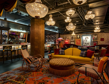 Cozy lounge with chandeliers, colorful seating, a bar area, and warm decor creating an intimate, stylish vibe throughout the space.