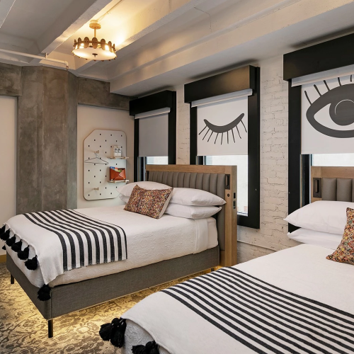 A stylish bedroom with a low platform bed, warm lighting, botanical wall art, a patterned rug, and a cozy seating nook.