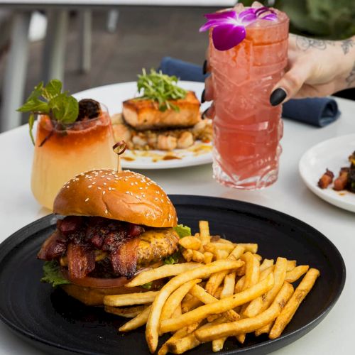 A plate of fries and two sauces, plus a side dish, with a glass of pink drink in the background.