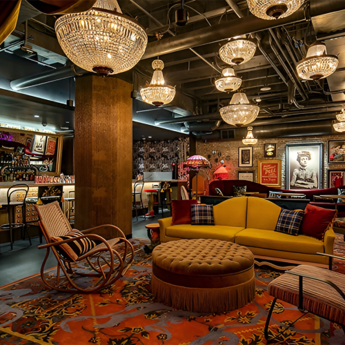 A cozy lounge with warm lighting, colorful cushions, and a mix of rustic and modern decor around a central seating area.