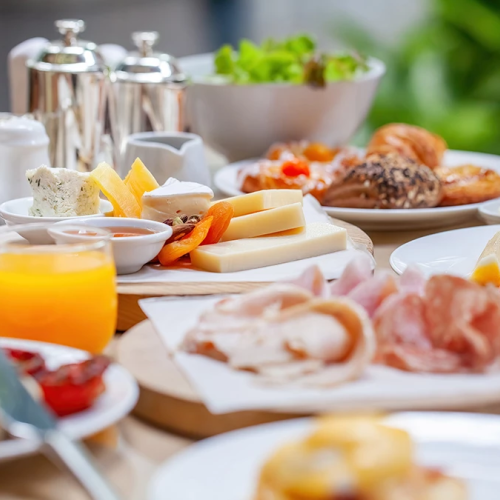 A lavish breakfast spread with cheeses, pastries, meats, fruit, juices, yogurt, and condiments on a sunlit table.