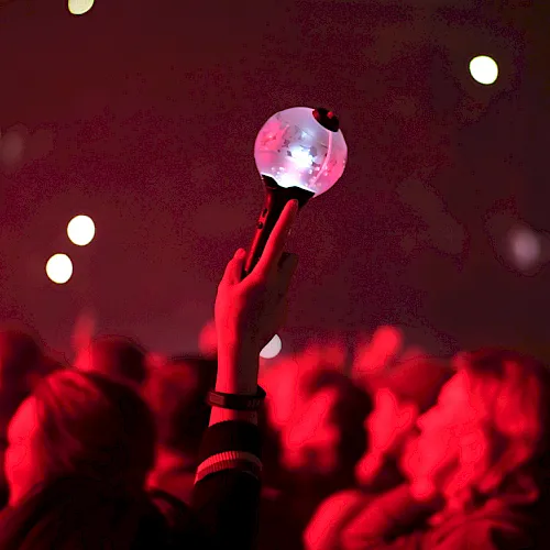 A concert crowd glows red as someone holds a sparkling disco-ball-like trophy aloft above the stage lights.