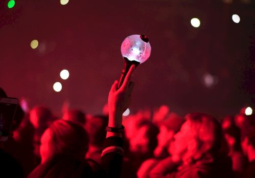 A concert crowd glows in red as someone holds up a sparkling disco-ball microphone-like trophy toward the stage lights.