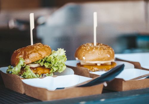 Two cheeseburgers in cardboard boxes with toothpicks, with lettuce and cheese visible, sitting on a restaurant tray.