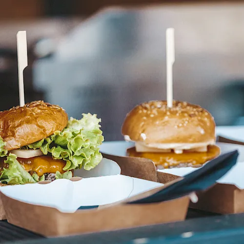 Two cheeseburgers in cardboard boxes with toothpicks, with lettuce and cheese visible, sitting on a restaurant tray.