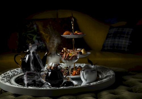 A spooky hookah-style tea set with smoking pots and a tiered platter of food and sweets on a tray.
